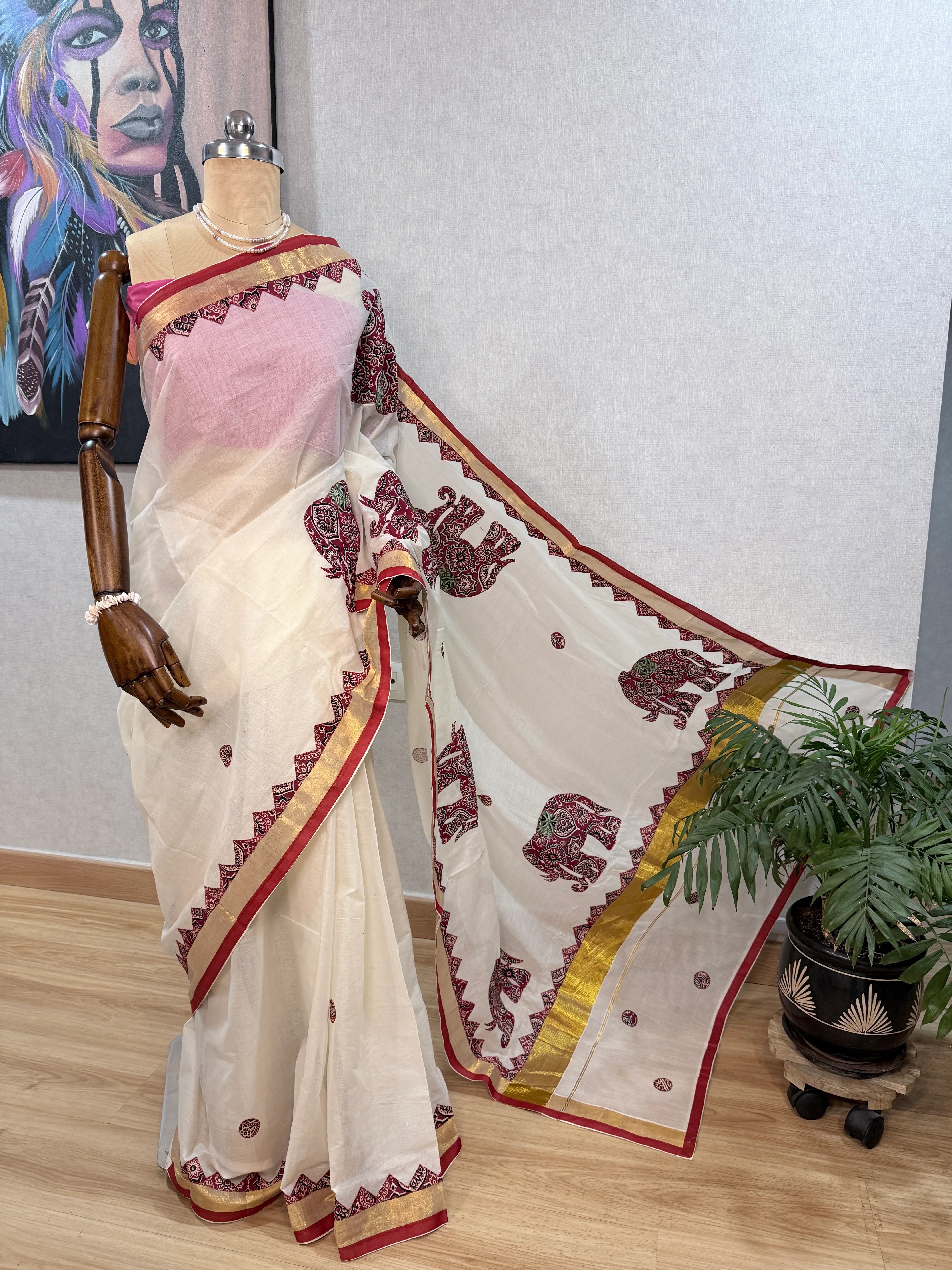 Same cream Kerala cotton saree on the mannequin, wider angle with the pallu spread out flat showing the full row of appliqué elephant motifs along the zari border.