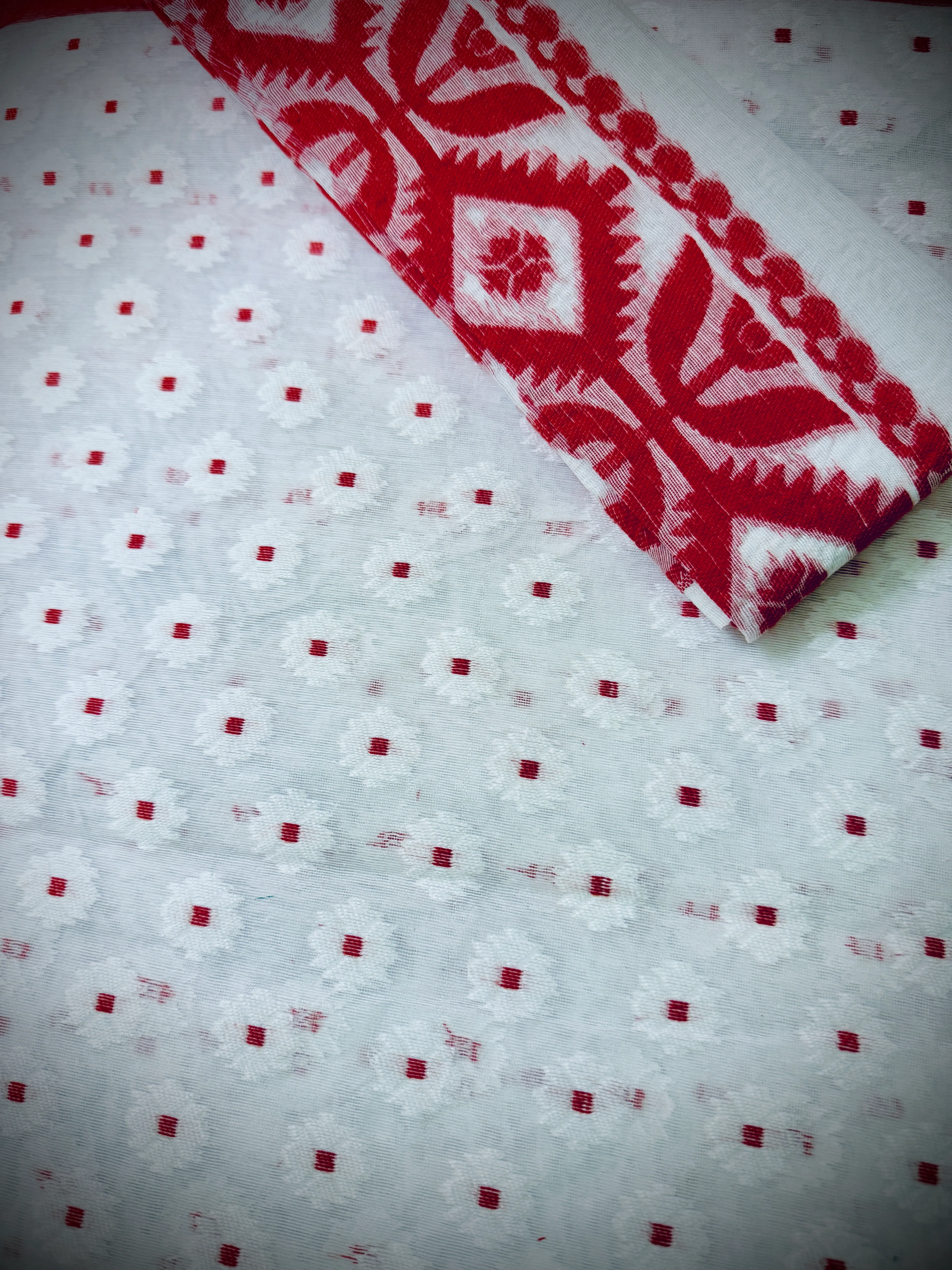 Dhakai jamdani saree fold showing the transition from the red ikat diamond body to a white ground with a red polka-dot motif.