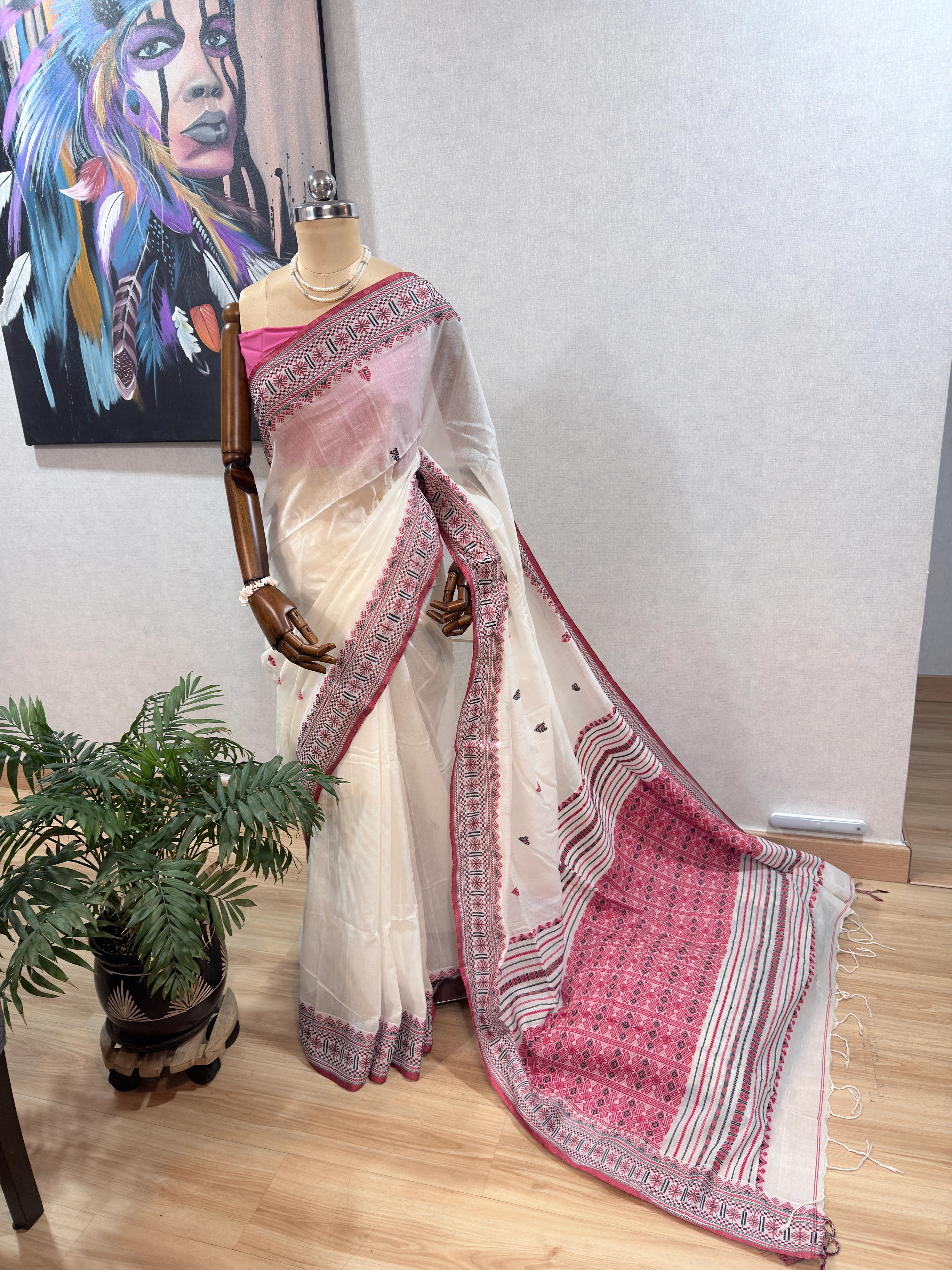 Close-up flat lay of the Dhonekhali saree's cream body scattered with small red and black leaf-shaped woven motifs, with its pink-and-black striped border visible at the edge.