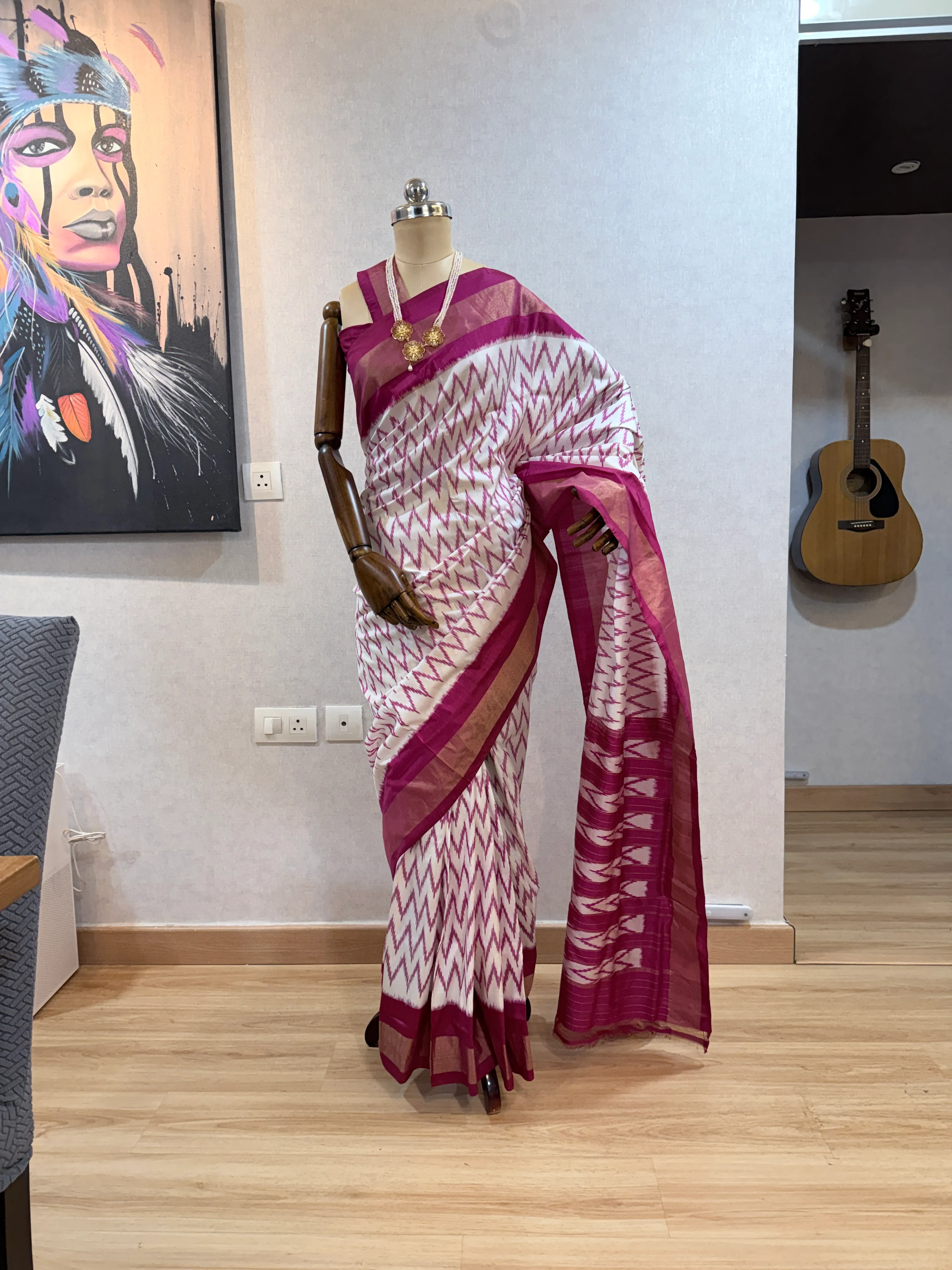Maroon-and-white chevron ikat saree on the mannequin from a slightly different angle, showing the pleated drape and gold border.