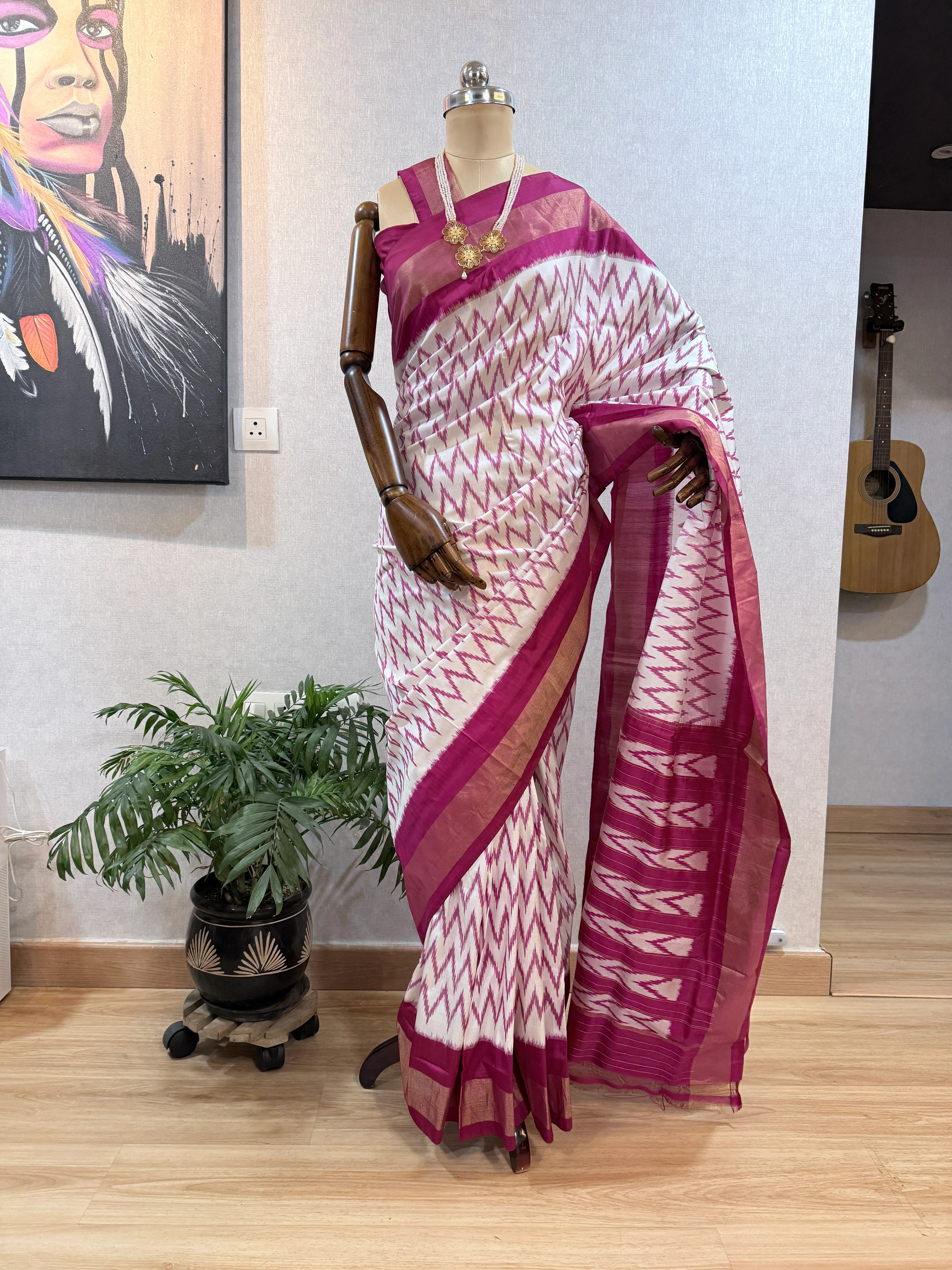 Maroon-and-white chevron ikat saree on the mannequin, wider framing including the guitar and room backdrop.