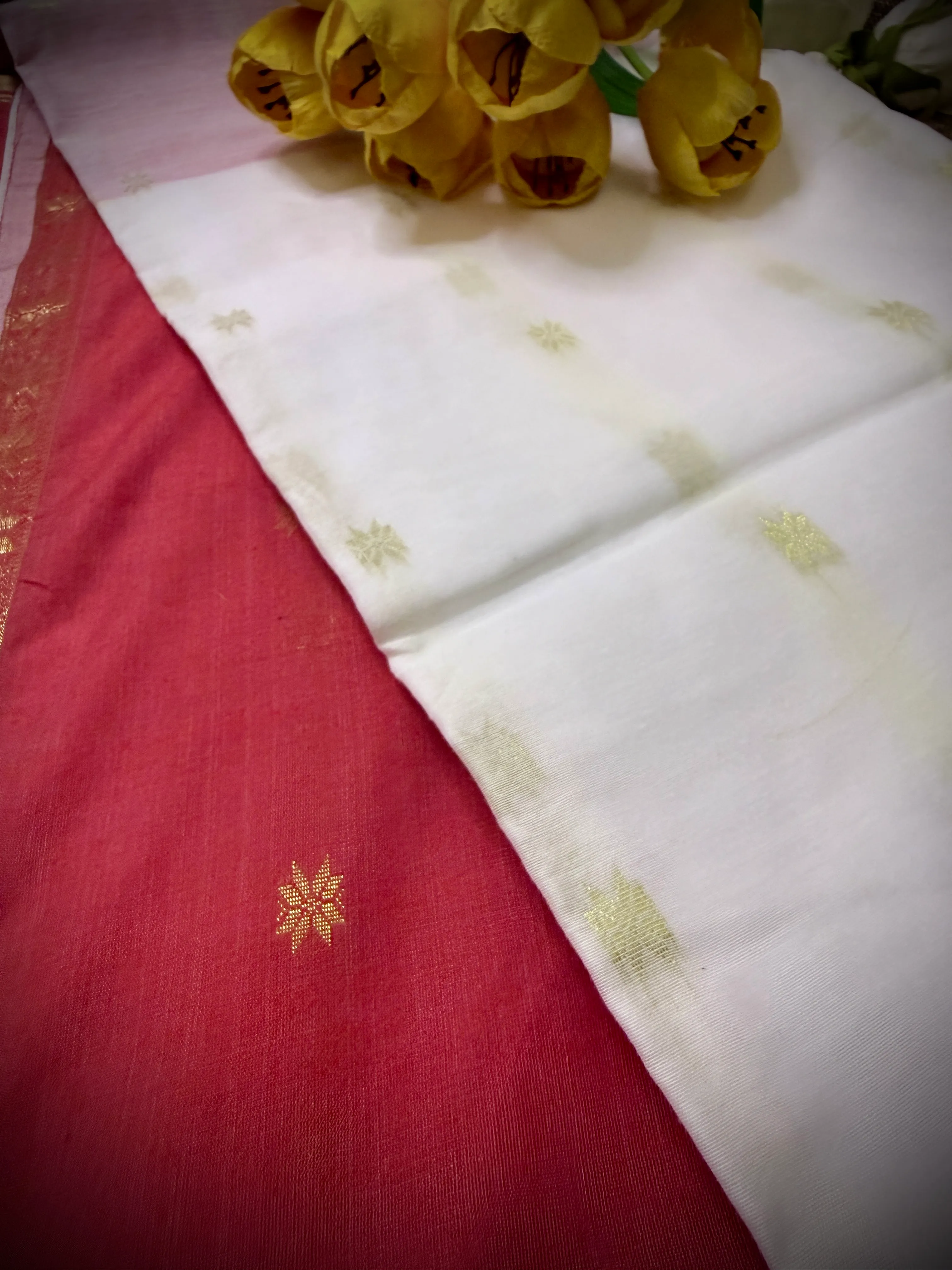 Folded white khadi cotton saree with gold star motifs and a pink-red border, styled with yellow tulips.