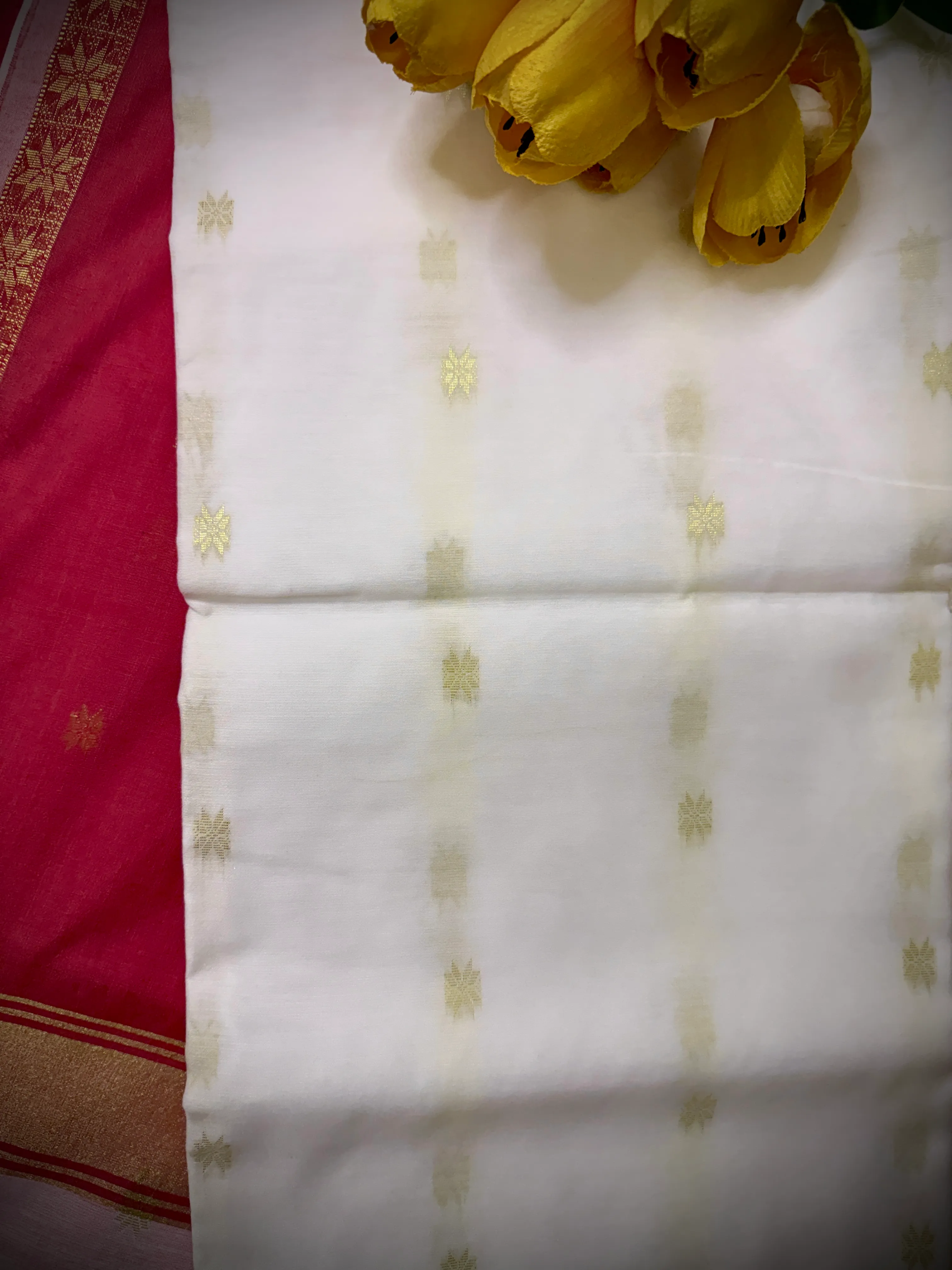 Folded white khadi cotton saree showing gold star motifs across two panels, styled with yellow tulips.