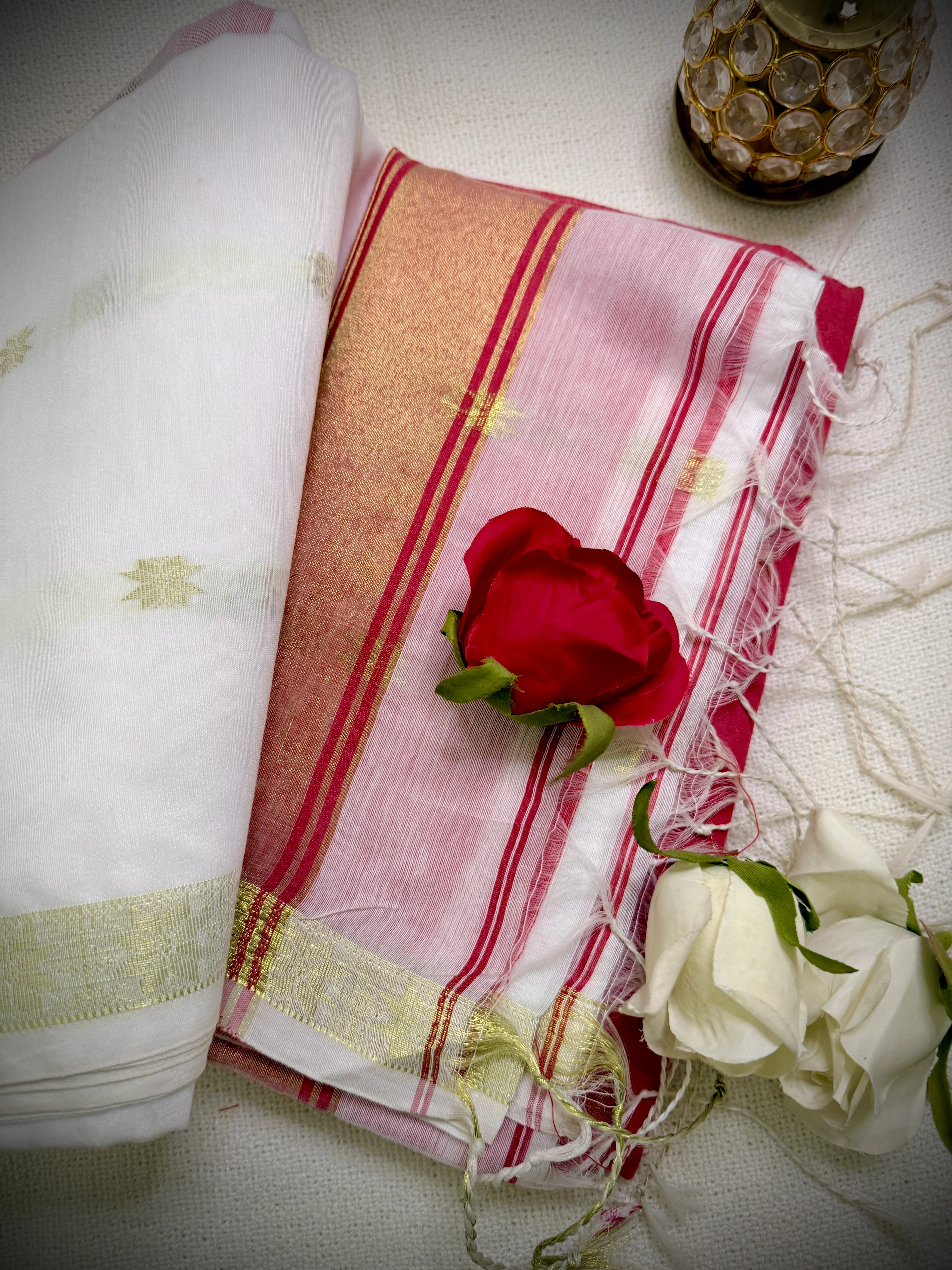 Folded khadi cotton saree in white and pink-red with a gold zari border, styled with a red rose and white roses.
